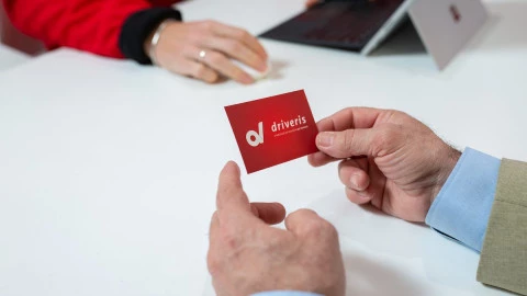 Manos de un cliente sosteniendo una tarjeta de Driveris durante una atención comercial en concesionario.