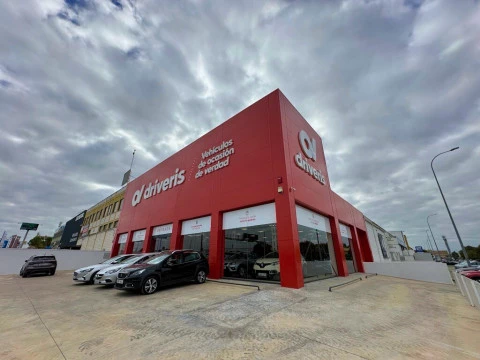 Fachada amplia y moderna de Driveris Carretera Amarilla con varios vehículos aparcados al exterior.