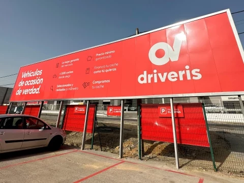 Entrada del concesionario Driveris con paneles publicitarios en rojo y logotipo visible