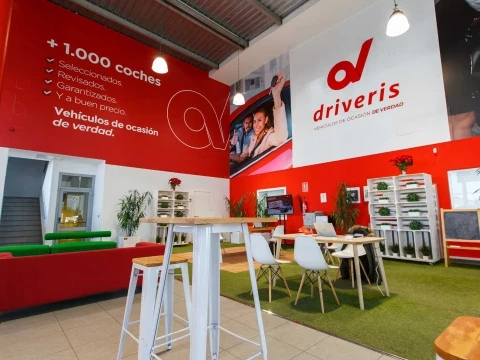 Área de atención al cliente en Driveris Sevilla con mesas altas y mural corporativo