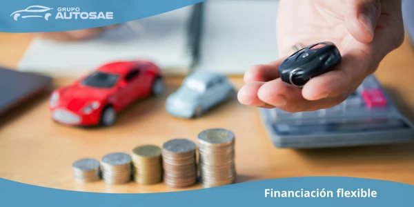 Mano sosteniendo la llave de un coche junto a monedas y miniaturas de vehículos, representando financiación flexible