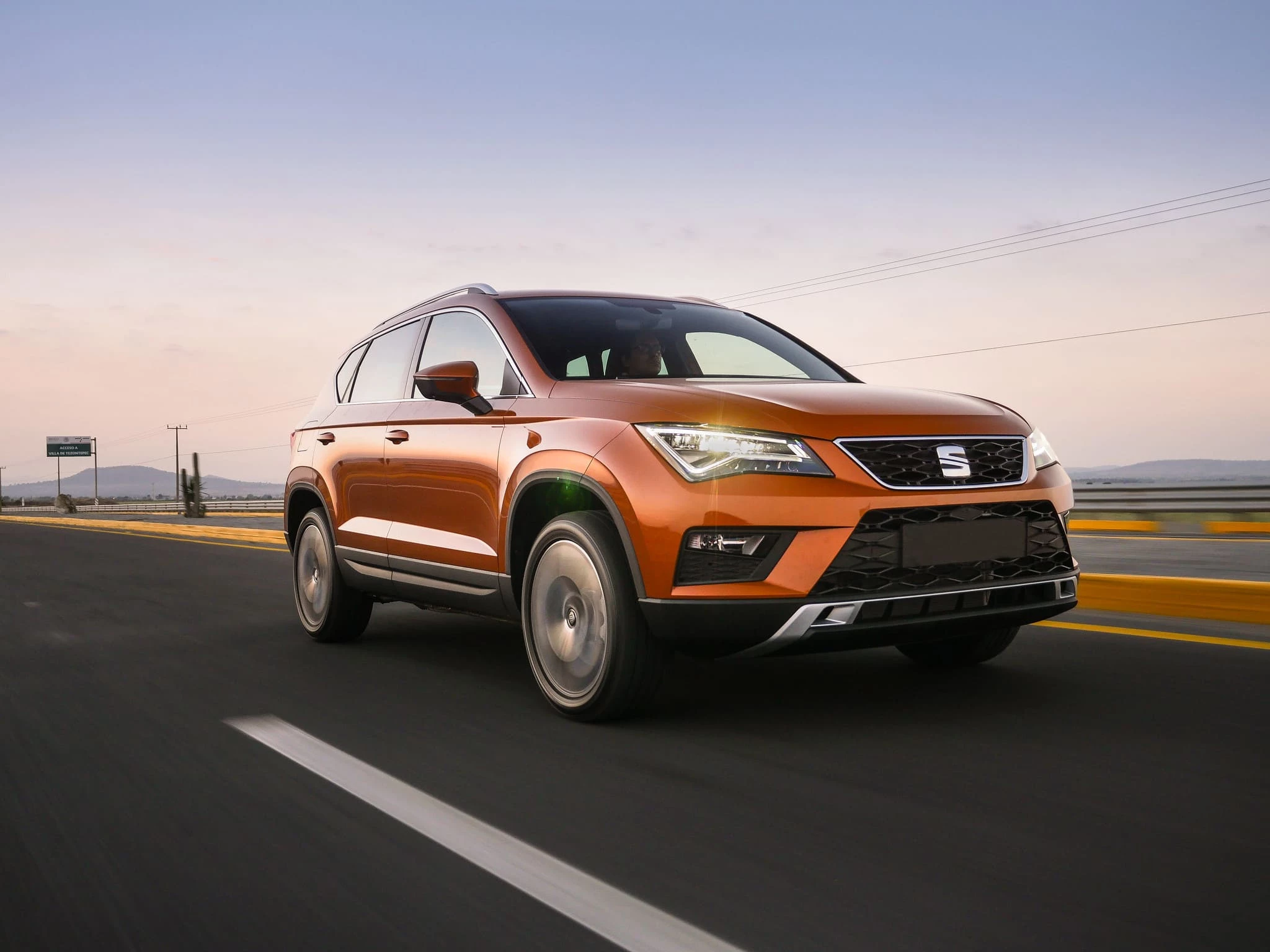 Vista frontal de un Seat Ateca naranja circulando por una carretera despejada