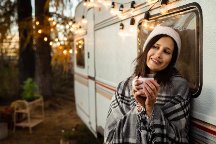 Mujer tomando un cafe caliente apoyada en la caravana