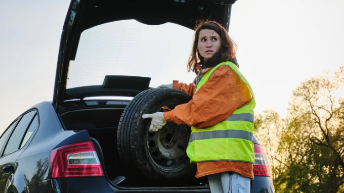 Mujer con su chaleco reflectante cambiando una rueda de coche